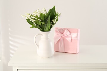 Beautiful lilies of the valley flowers and gift on white table