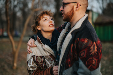 A couple embraces outdoors, wearing warm jackets, sharing a genuine and affectionate moment in nature.