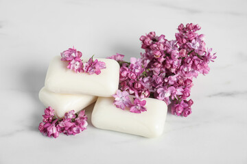 Soap bars and lilac flowers on white marble table, closeup