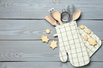 Different kitchen utensils in oven mitten and star shaped cookies on light grey wooden table, flat...