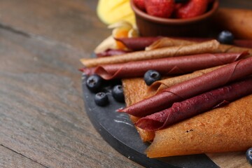 Delicious fruit leather rolls and berries on wooden table, closeup. Space for text