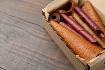 Delicious fruit leather rolls in cardboard box on wooden table, closeup. Space for text