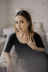 Portrait of a young woman with makeup and jewelry sitting on a couch indoors