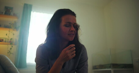 Woman sitting on a bed, crying with her head down, overwhelmed by grief and emotional pain,...