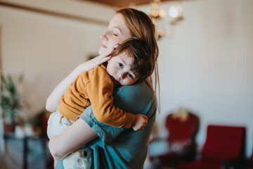 An intimate scene showing a loving embrace between a woman and a child in a cozy indoor...