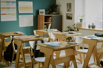 Warmly lit classroom with neatly arranged wooden desks, minimalistic decor, and educational materials on walls, offering inviting and organized learning environment