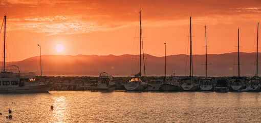 Orange sunset over a seaport with docked sailboats and motorboats, creating a picturesque marine landscape