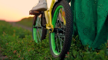 Fototapeta premium Childhood dream to ride bike. Young mother teaches child to keep balance while sitting on bicycle. Happy family life mom baby, Parental support. Mom teaches her little kid to ride bicycle, sunset