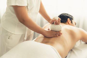 Hot herbal ball spa massage body treatment, masseur gently compresses herb bag on man body....