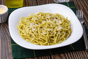 Italian pasta spaghetti on a plate with pesto sauce and parmesan cheese
