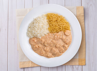 Shrimp strogonoff with rice and straw potato over wooden table