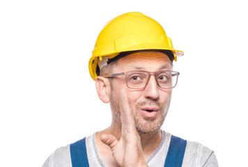 Middle-aged construction worker holding hand near mouth and telling secret, isolated on white background. Gossip concept. Craftsman against white wall