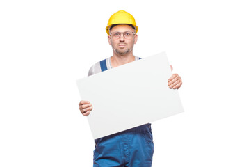 Promoting construction worker holding white board, isolated on white background. Amused repairman showing blank empty paper billboard with blank space for text. Craftsman against white wall