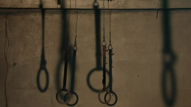 Two dark hanging straps slowly twist and turn. A striking blue/teal rim light dramatically defines their edges against a mysterious, blurred background. Close-up detail.