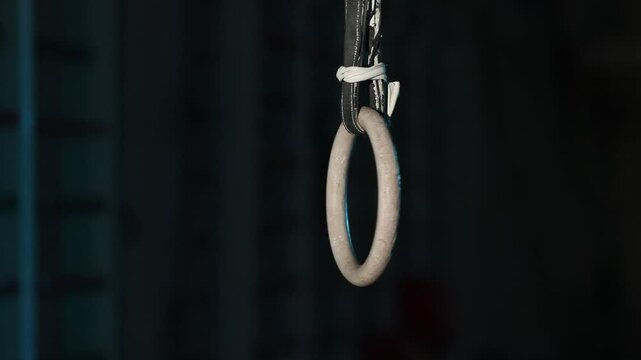 Two dark hanging straps slowly twist and turn. A striking blue/teal rim light dramatically defines their edges against a mysterious, blurred background. Close-up detail.