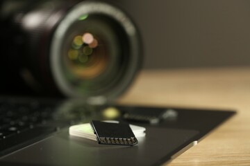 SD memory card, holder, laptop and photo camera on wooden table, closeup