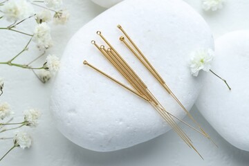 Acupuncture needles, pebble stones and flowers on light table, flat lay