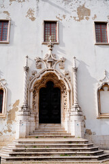 A historic building with a grand entrance featuring ornate architectural details. The facade shows signs of wear with peeling paint, and the entrance is flanked by decorative columns and windows.
