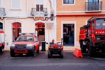 A row of emergency vehicles parked in a colorful urban setting. The vehicles include a fire truck, a red SUV, and an all-terrain vehicle, with a backdrop of charming buildings. © luengo_ua