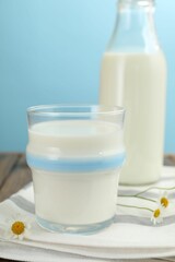 Fresh milk and flowers on wooden table against light blue background, closeup
