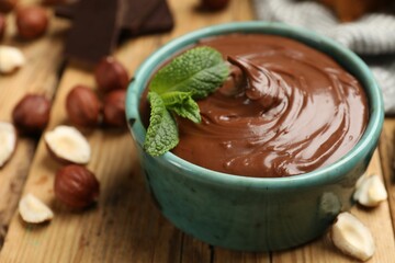 Tasty chocolate hazelnut spread with mint and nuts on wooden table, closeup