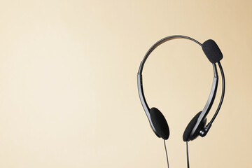 Headset with microphone in air on beige background, space for text