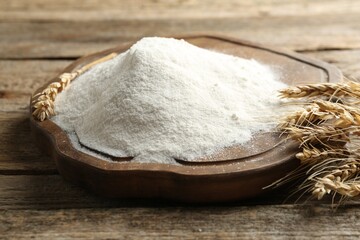 Wheat flour and spikelets on wooden table, closeup