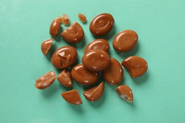 Many tasty caramel candies on turquoise background, flat lay