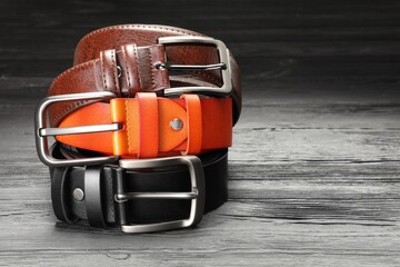 Three leather belts on wooden table, closeup. Space for text