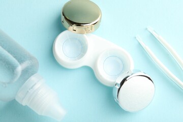 Contact lenses in case, solution and tweezers on light turquoise background, flat lay