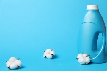 Bottle of fabric softener and cotton flowers on light blue background, space for text