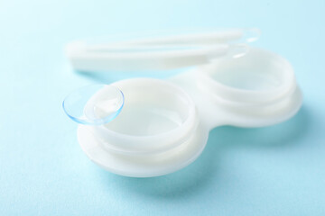 Contact lenses, case and tweezers on light blue background, closeup