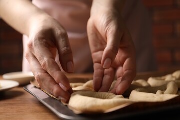 Woman putting uncooked pretzel onto baking dish at wooden table, closeup