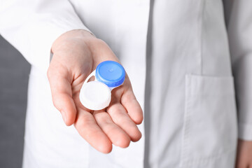 Fototapeta premium Doctor holding case with contact lenses on grey background, closeup