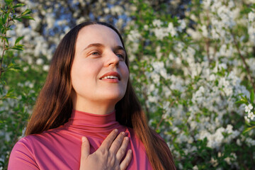 Woman breathes easily outdoors among white flowers, serene and free from allergies, enjoying the fresh spring air and nature.