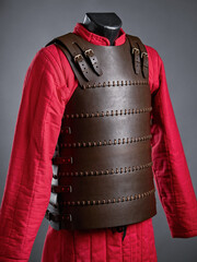 A dark leather brigandine armor featured on a mannequin with red undergarment, emphasizing medieval...