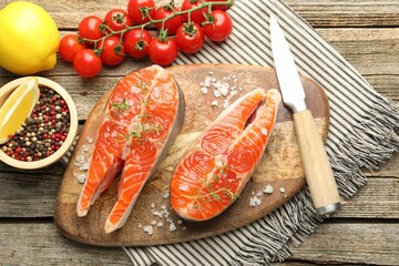 Seafood. Salmon steaks, spices, tomatoes, lemons and knife on wooden table, flat lay