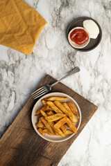 Crispy, golden, seasoned, homestyle french fries on a plate with a fork on wood cutting board and marbled background. Vertical