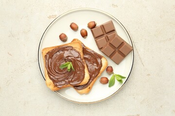 Toasts with tasty chocolate spread, pieces, mint and hazelnuts on light table, top view