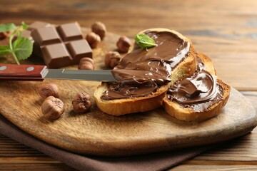 Toasts with tasty chocolate spread, pieces, mint and hazelnuts on wooden table, closeup