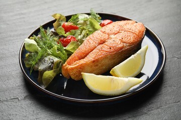 Seafood. Tasty salmon steak served with salad and lemon on black table, closeup