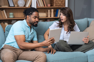 Young couple working remotely at home, analyzing documents and data, using laptop in cozy modern...