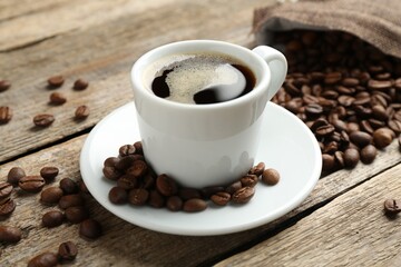 Aromatic coffee in cup and beans on wooden table, closeup