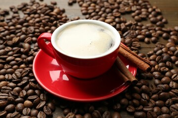 Aromatic coffee in cup, beans and cinnamon on table, closeup