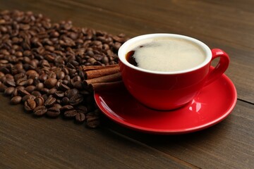Aromatic coffee in cup, beans and cinnamon on wooden table, closeup