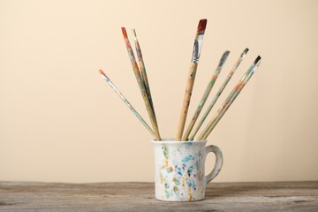 Brush with color paints in cup on wooden table