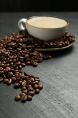 Aromatic coffee in cup and beans on black table, closeup