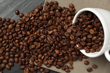 Aromatic coffee beans and overturned cup on black table, above view