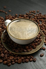 Aromatic coffee in cup and beans on black table, closeup