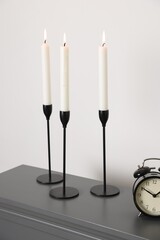 Stylish candlesticks with burning candles and alarm clock on fireplace near white wall indoors